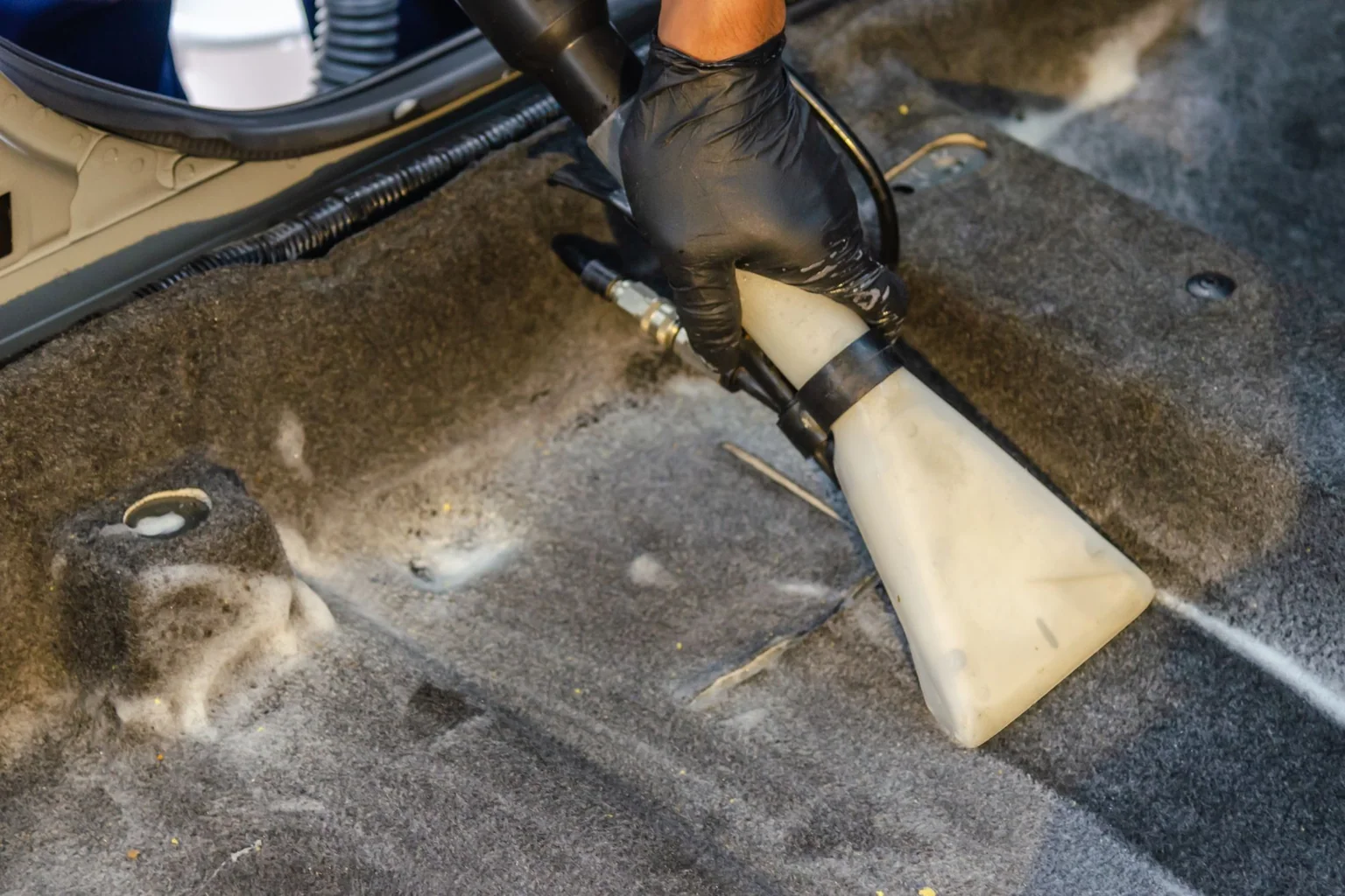 Gloved hand using a vacuum extractor nozzle on the carpet inside a car