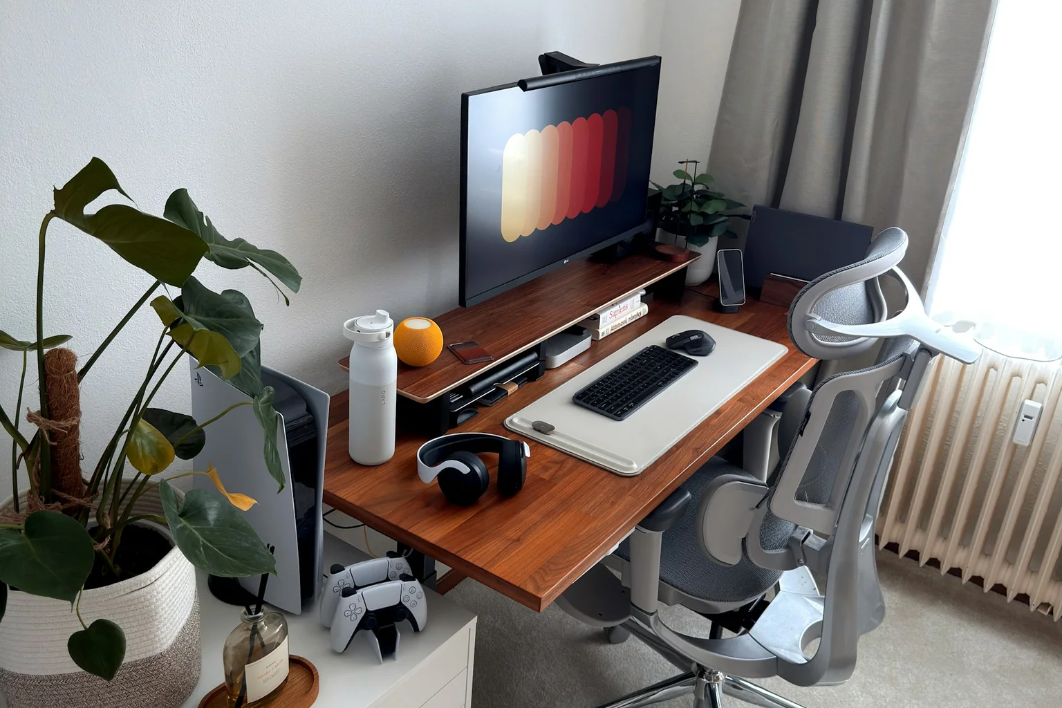 Organized home office desk with monitor, keyboard, headphones, charging stand and ergonomic chair