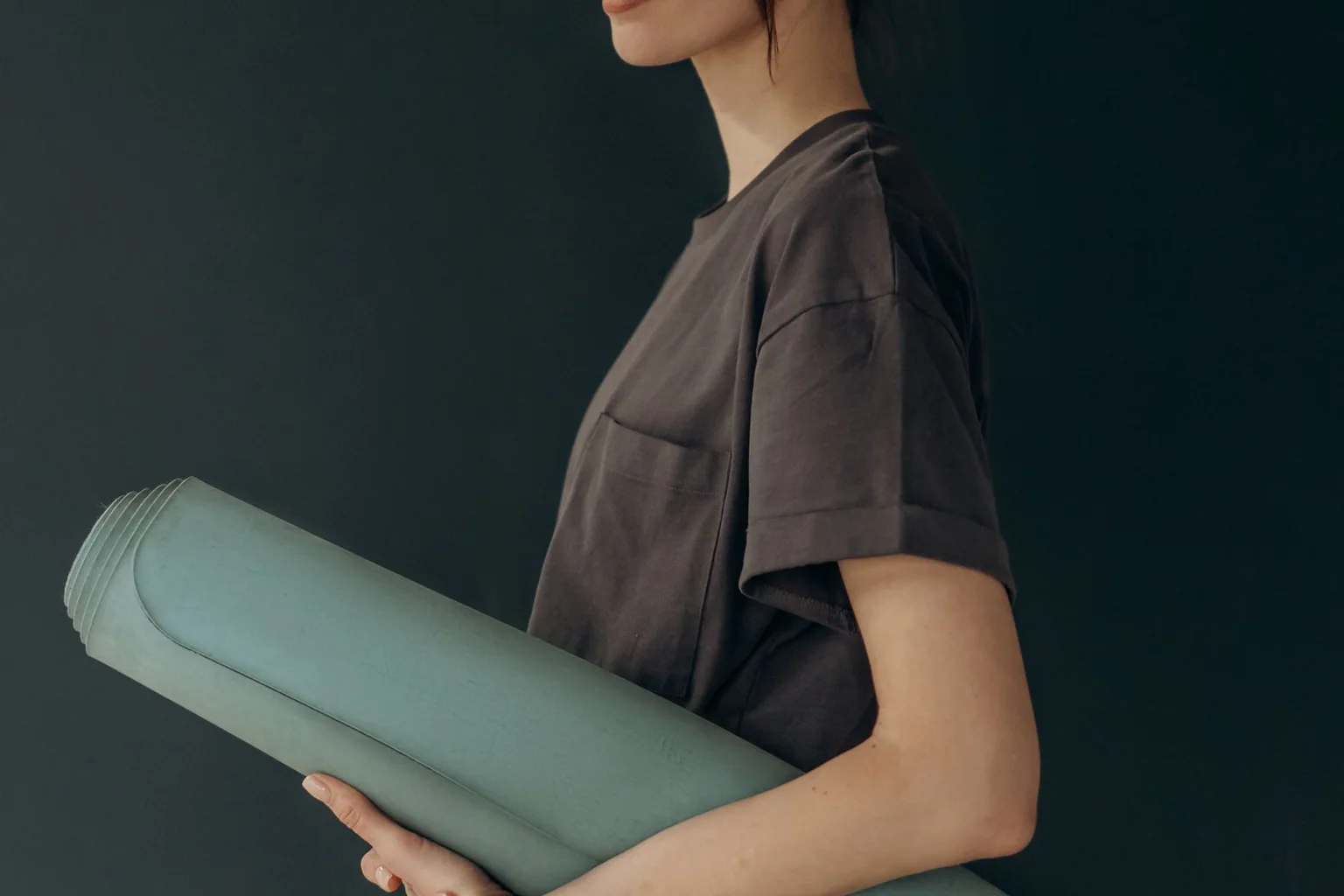 Person in dark clothing carrying a rolled green yoga mat
