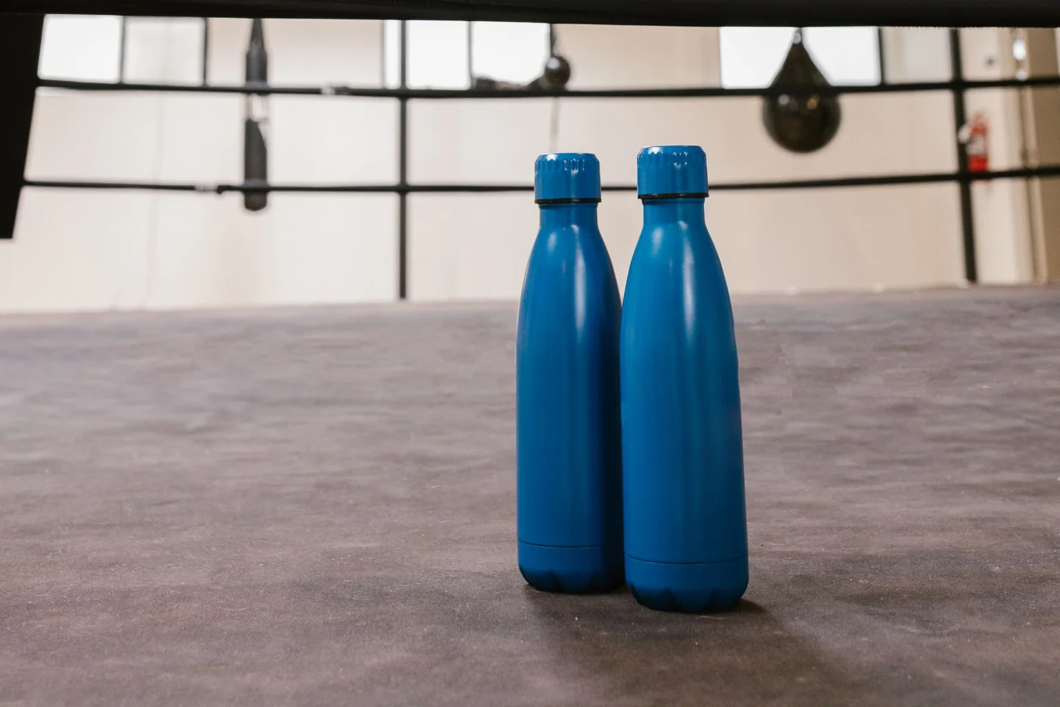 Two blue reusable water bottles standing inside a boxing gym